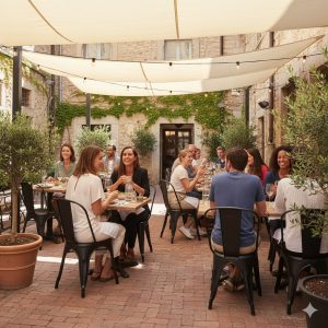 Super-Seat | Zwarte metalen stapelstoelen bij houten tafels op een terras met bakstenen vloer en planten. | Horecameubilair