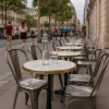 Super-Seat | Metalen vintage Lix stoelen en tafels bij een Parijse stoep; glazen flessen op houten tafelbladen, mensen op achtergrond. | Horecameubilair