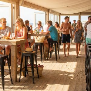 Super-Seat | Zwarte metalen Lix barkrukken, houten tafels en stoelen, lichtinval, uitzicht op zee, groepen mensen. | Horecameubilair