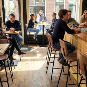 Super-Seat | Barkrukken in cognac leer en metaal bij houten tafels in café met bakstenen muren, veel licht. | Horecameubilair
