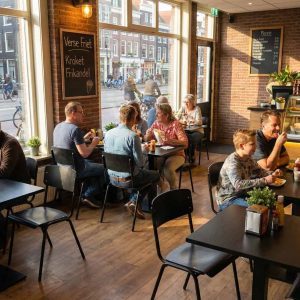 Super-Seat | Vanitas vintage schoolstoelen zwart in café Zwarte metalen stoelen, houten tafels; grote ramen, licht en gezellig. | Horecameubilair