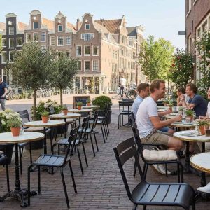 Super-Seat | Zwarte metalen stapelstoelen en tafels op een klinkerterras met planten en stadszicht. | Horecameubilair