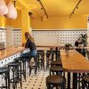 Super-Seat | Bentwood Café-interieur | Het café toont zwarte Thonet-barkrukjes aan een houten toonbank, met gele muren en een geblokte vloer. | Horecameubilair
