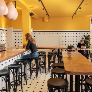 Super-Seat | Bentwood Café-interieur | Het café toont zwarte Thonet-barkrukjes aan een houten toonbank, met gele muren en een geblokte vloer. | Horecameubilair