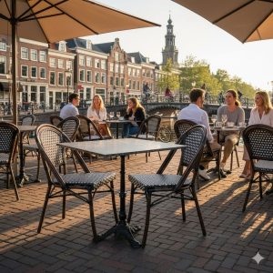 Super-Seat | Zwarte rieten stapelstoelen en bistrotafels op stenen terras, mensen genieten van de zon. | Horecameubilair
