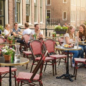 Super-Seat |Rode rieten stapelstoelen en houten terras tafels buiten langs kinderkopstraat. | Horecameubilair