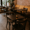 Super-Seat | Stoelen, tafels en meer | Donkere houten tafels, bruine Thon gebogen houten stoelen met spijlen, gele bank, bakstenen muur. | Horecameubilair