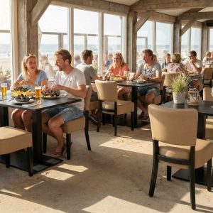 Super-Seat | Lisa Rome horeca stoelen Taupe | Zandkleurige stoffen stoelen rond houten tafels, zonlicht door ramen met uitzicht op het strand. | Horecameubilair