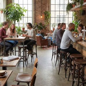 Super-Seat | Houten stoelen, zwarte bistro tafels, houten bar met krukken in licht café met planten en ramen. | Horecameubilair