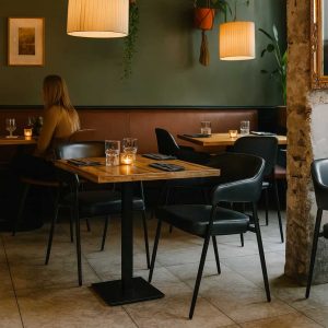 Super-Seat | Een modern restaurant met donkergroene muren, houten gedekte tafels, zwart en hout. Houten tafels, zwarte Maxwell horeca armstoelen, glazen en servetten. | Horecameubilair