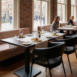 Super-Seat | Zwarte Maxwell stoelen van stof en metaal, houten tafels, bakstenen muur in zonnig restaurant. | Horecameubilair