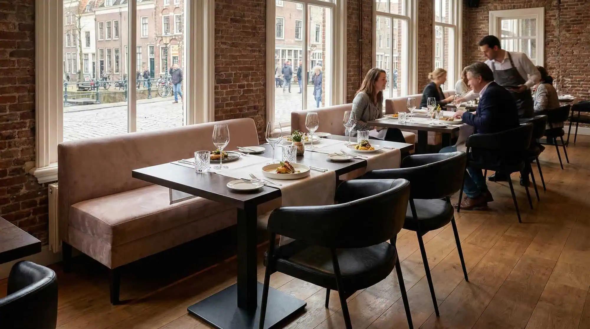 Super-Seat | Zwarte Maxwell stoelen van stof en metaal, houten tafels, bakstenen muur in zonnig restaurant. | Horecameubilair