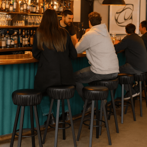 Super-Seat | Zwarte industriële barkrukken van metaal, vier mensen aan houten bar met flessen en glazen. | Horecameubilair