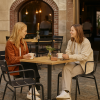 Super-Seat |Twee vrouwen op zwarte metalen terras armstoelen aan tafel met bloemenvaas; omringd door lege stoelen; bakstenen muur. | Horecameubilair