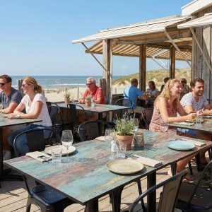 Super-Seat | Terras tafelbladen roest en koper Bruine HPL tafels 70x70cm, houten terrasvloer, omringd door strand, stoelen in neutrale tinten. | Horecameubilair