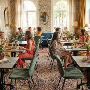 Super-Seat |Groepen rond HPL roest-koperen tafels, blauwe banken, bloemenbehang & grote ramen in stijlvol café. | Horecameubilair