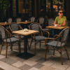 Super-Seat | Wicker Horeca Terrasstoelen Zwart | Zwarte wickerstoelen met armleuningen, metalen tafels op terras, vrouw in groen, koffie. | Horecameubilair
