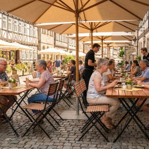 Super-Seat | Kunststof rotan terrasstoelen Prada | Zwarte kunststof rotan klapstoelen en tafels op straat, houten barkrukken zichtbaar. | Horecameubilair