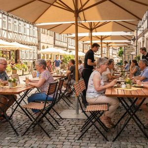 Super-Seat | Kunststof rotan terrasstoelen Prada | Zwarte kunststof rotan klapstoelen en tafels op straat, houten barkrukken zichtbaar. | Horecameubilair