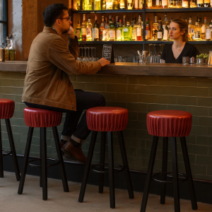 Super-Seat | Rode industriële barkrukken van metaal bij bar, man belt, vrouw achter bar, flessen op planken. | Horecameubilair
