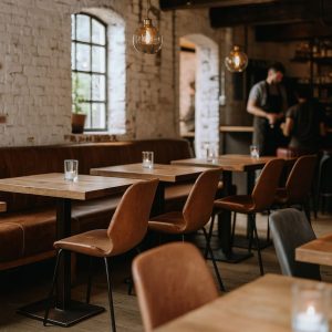 Super-Seat | Houten tafels, bruine leren stoelen (cognac), houten barkrukken, witte bakstenen muur, stoffen bank. | Horecameubilair