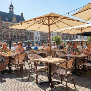 Super-Seat | Marylin Parijse horeca terras | Boho beige stoelen, armstoelen en tafels van hout/metaal op kinderkopjesplein met parasols. | Horecameubilair