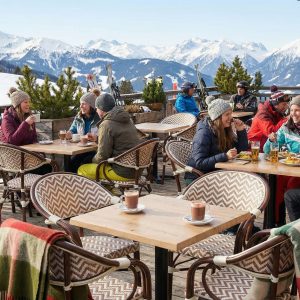 Super-Seat | Boho beige stoelen met armdekens, houten tafels en krukken op besneeuwd terras, mensen in winterkleding. | Horecameubilair