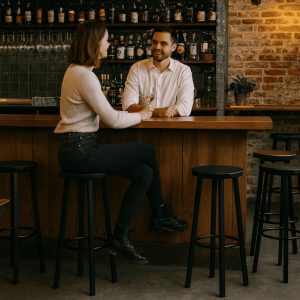 Super-Seat | Zwarte metalen barkrukken, houten bar, bakstenen muur, flessen en glazen op plank. | Horecameubilair