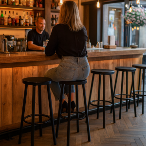 Super-Seat | Zwarte metalen barkrukken aan houten bar, warme sfeer en lege barkrukken. | Horecameubilair