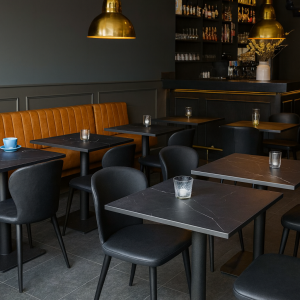 Super-Seat | Een modern café-interieur | Zwarte melamine tafels, beige bank, gouden lampen, flessenrek en blauwe koffiekop op tafel. | Horecameubilair