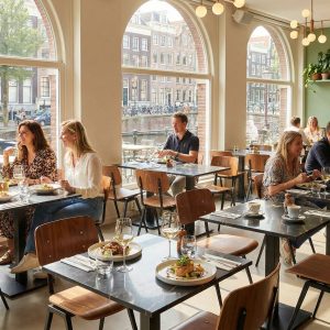 Super-Seat | Zwarte marmer look tafels, houten stoelen, planten, lichte ruimte met grote ramen. | Horecameubilair