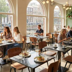 Super-Seat | Zwarte marmer look tafels, houten stoelen, planten, lichte ruimte met grote ramen. | Horecameubilair