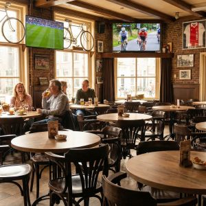 Super-Seat |Houten tafels, stoelen en barkrukken; warme eikenkleur in sportbar met fietsen aan de muur. | Horecameubilair