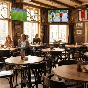 Super-Seat |Houten tafels, stoelen en barkrukken; warme eikenkleur in sportbar met fietsen aan de muur. | Horecameubilair