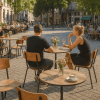 Super-Seat | Twee personen aan ronde eiken HPL tafel, zwarte metalen stoelen, zonovergoten terras. | Horecameubilair