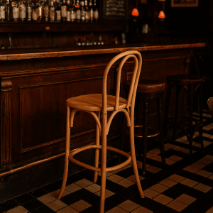 Super-Seat | Vienna Thon no 18 houten barkrukken | Naturel hout, gebogen rugleuning, bij donkerhouten bar op zwart-wit tegelvloer. | Horecameubilair