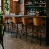 Super-Seat | Een bar met een stenen vloer, bakstenen muur en vier New Yorkse design barkrukken hout zwart leer. | Vier zwarte leren barkrukken met houten poten; bar met stenen vloer en binnenmuur. | Horecameubilair