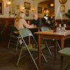 Super-Seat | FieldFold vintage metalen leger-klapstoelen legergroen in houten café | Legergroene metalen klapstoelen, houten tafels, glazen bekers, bruine fles. | Horecameubilair