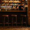 Super-Seat | Jazz retro horeca design stapelstoelen fluweel mokka Drie mokka-fluwelen stoelen bij houten bar, flessen en kranen op houten rekken. | Horecameubilair