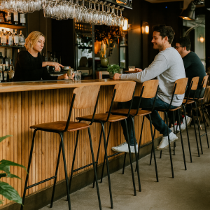 Super-Seat | Man zit op mokkabruine fluwelen stapelstoel aan houten bar, flessen op plank erboven. | Horecameubilair