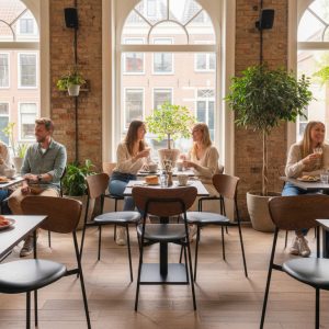 Super-Seat | Bruin eiken melamine tafelbladen 67x67cm Bruin eiken tafels, metalen stoelen, grote ramen, bakstenen muren, groene planten. | Horecameubilair