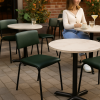 Super-Seat | Vanitas stapelstoelen groen Groene Vanitas metalen stoelen, houten tafels, vrouw met beker tussen planten op bakstenen terras. | Horecameubilair