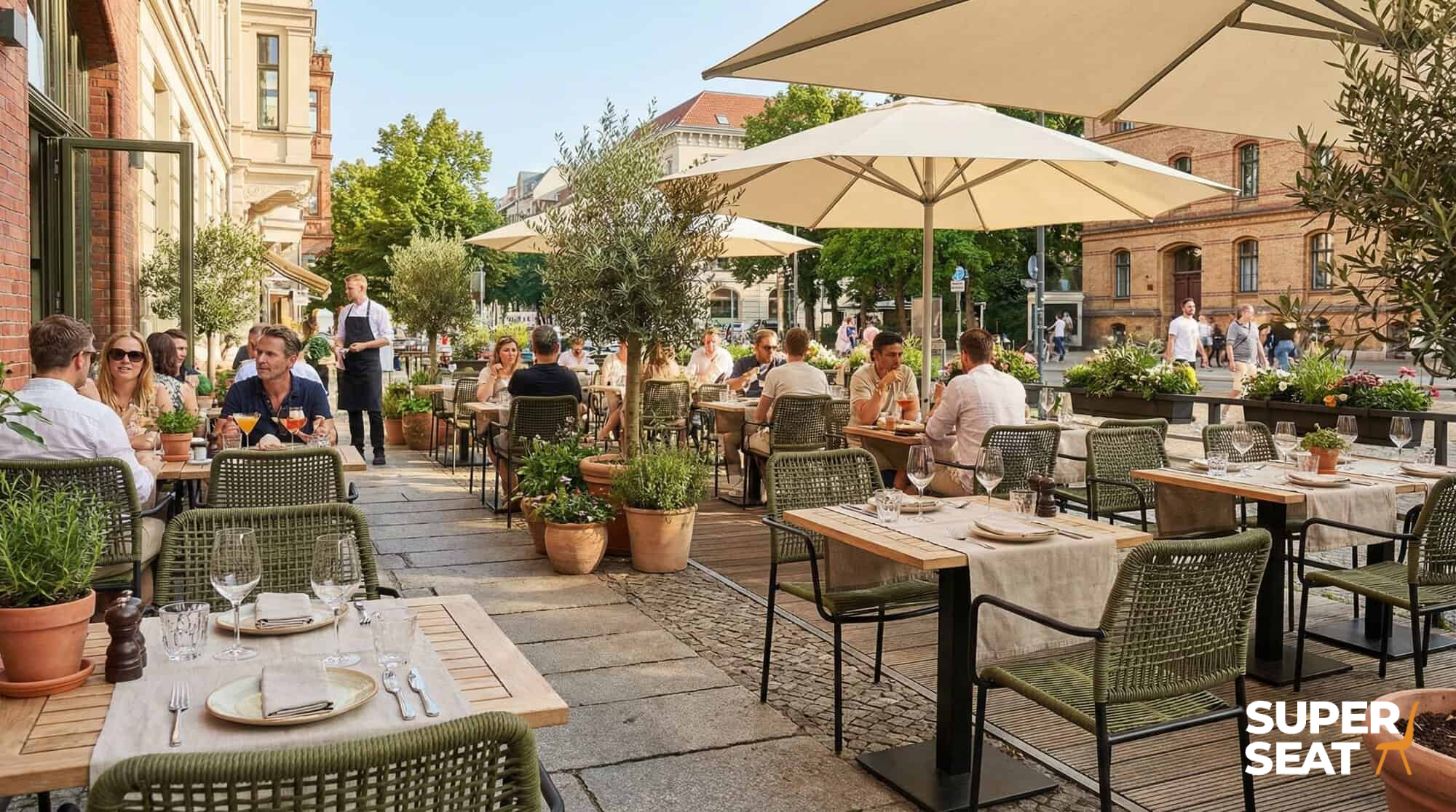 Super-Seat | Goedkope horecastoelen Harper groen Groene stapelstoelen met arm, metalen frame, bij houten tafels op zonnig terras met parasols. | Horecameubilair