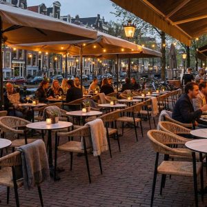 Super-Seat | Restaurant aan het water Houten tafels, grijze en zwarte stoelen, houten barkrukken op stenen terras onder grote witte parasols. | Horecameubilair