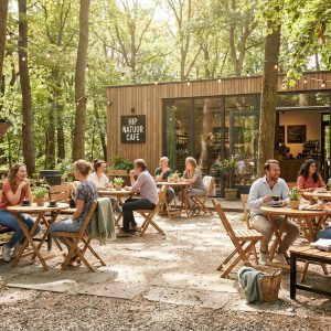 Super-Seat | HIP NATUR CAFE | Buiten staan houten tafels, stoelen en picknicktafels van hout in zon en schaduw tussen bomen. | Horecameubilair
